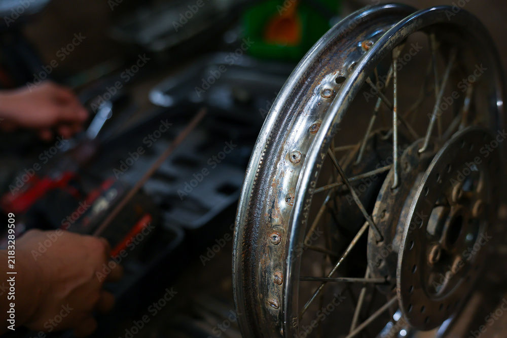 Fototapeta premium Motorcycle wheel repair dim workshop mechanic hands tool close up showing spoke rim maintenance with blurred workbench, gritty garage setting, focused manual labor