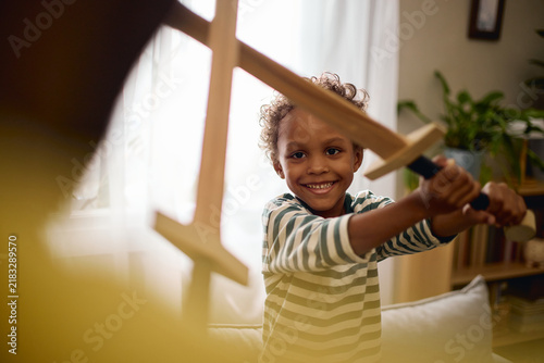 Foto African American boy smiling while playing wooden sword fight with father at home