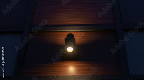 Konstfotografi Small wall lantern emitting warm light on dark wooden panel facade with raindrop