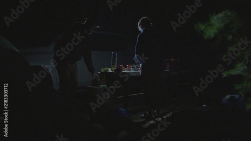 Two men camping at night and walk around the camping site at night with the car parked nearby