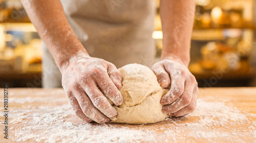 Obraz na płótnie Experienced baker's hands skillfully kneading fresh, soft dough on a rustic wooden table dusted with white flour
