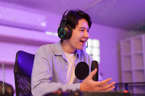 Foto Asian male streamer wearing headset talking into microphone during live stream