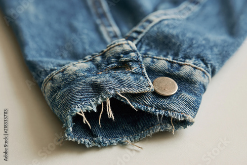 Close-up of frayed denim jacket cuff with button detail  
