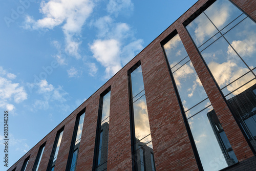 Modern brick building with large glass windows and balcony against blue sky with clouds