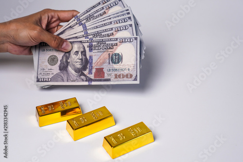 Obraz na plátne A hand holding a stack of US$100 banknotes and three gold bars.