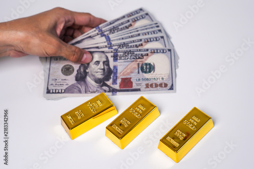 Картината върху платно A hand holding a stack of US$100 banknotes and three gold bars.