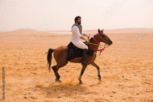 Принти на полотні Authentic Arab horseman in traditional keffiyeh scarf riding bay horse at full g