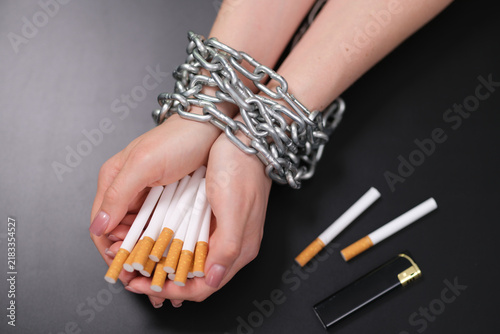 Konstfotografi Close view of hands wrapped in heavy metal chain while holding cigarettes beside