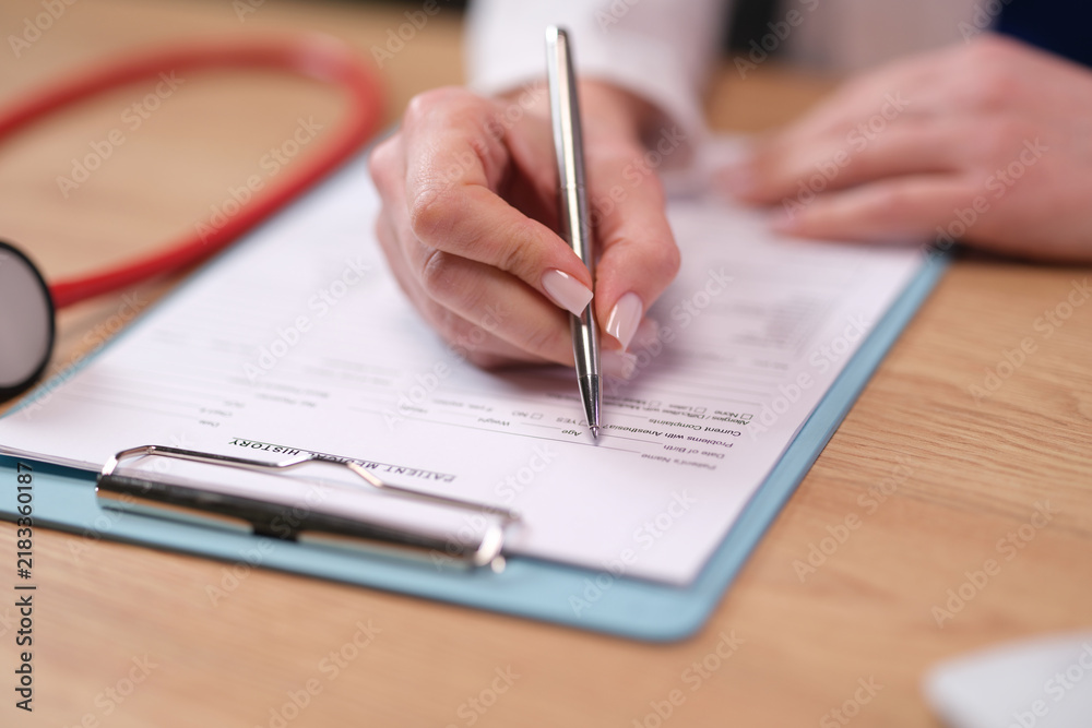 Obraz premium Medical professional fills printed form near stethoscope on desk. Doctor hand writes patient information completing clinical medical history with pen
