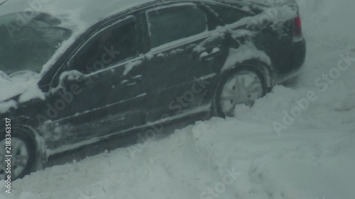 Automobile stuck in deep snowdrift during winter blizzard condition, front wheel spinning unable to gain traction, challenging road situation, slow motion