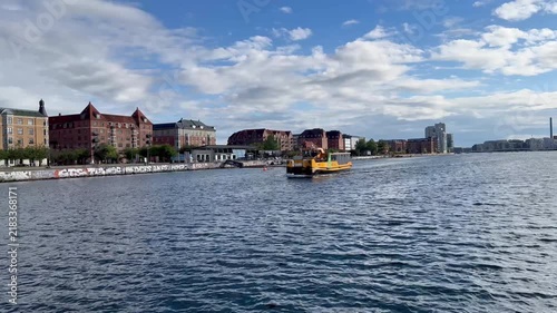 Yellow public transport boat, also known as a Harbour Bus, navigating the waters of Islands Brygge in Copenhagen, Denmark, passing by the city's waterfront with its distinct architecture - stock video