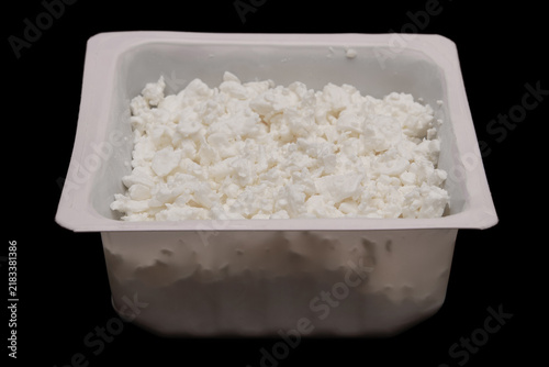 Cottage cheese in container isolated on black background. Side view. Pressed milk solids
