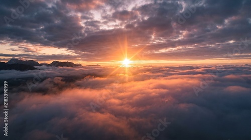 Sunburst shining over a dense layer of clouds above mountain peaks at sunrise with mountain summits visible
