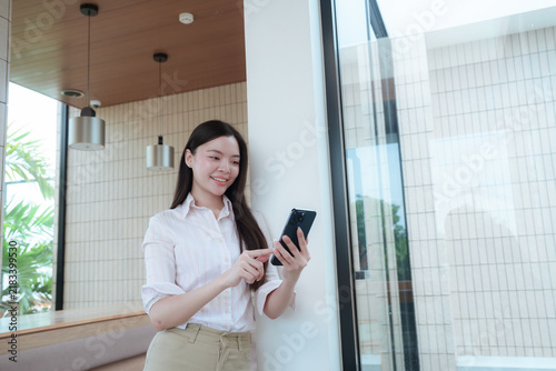 Confident Asian businesswoman using a smartphone in a modern office, representing professional communication, digital technology, contemporary business, and corporate lifestyle.
