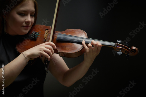 Young adult Caucasian woman playing violin during classical music performance. Image suitable for arts education, orchestra advertising, and acoustic concert promotion