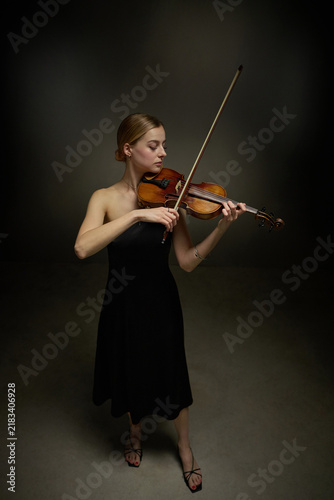 Vertical shot of young adult Caucasian woman playing violin during classical music performance. Image suitable for arts education, concert promotion, orchestral marketing materials