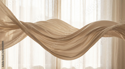 Flowing beige silk fabric wave against a soft light curtain background