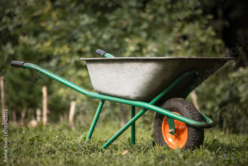 Garden scene with  wheelbarrow and wooden posts in a grassy field, outdoor work area.