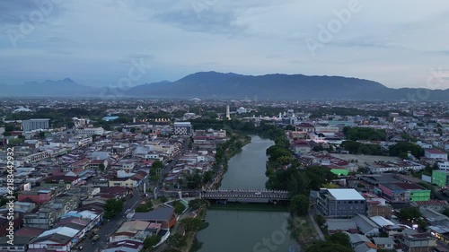Banda Aceh, Indonesia : Orbit aerial drone footage of riverside mosque and residential area in Banda Aceh of Sumatera, Indonesia toward Baiturrahman Grand Mosque and mountain under cloudy sunset sky