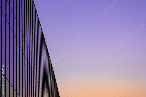 A minimalist architectural view of a modern glass building facade with geometric lines against a colorful purple and orange sunset sky.concept building business