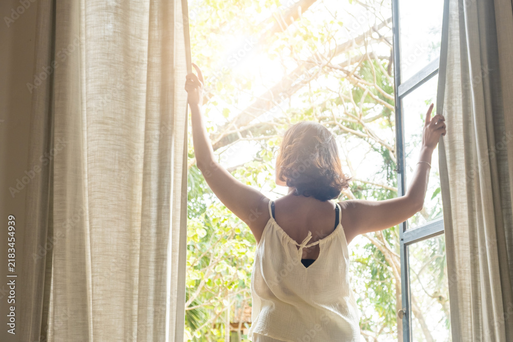 Obraz premium The woman was at the window in the bedroom. She opened the curtains on the window. In the morning and she looks at the view of mountains and trees at sunrise. 