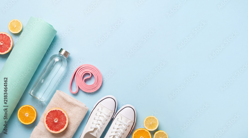 Obraz premium Fitness accessories including a yoga mat, sports shoes, water bottle, and fresh citrus on a blue background