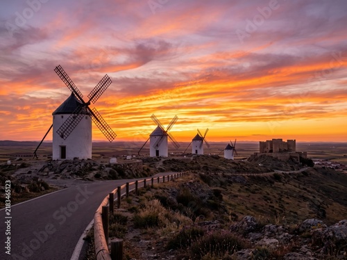 Traditional white windmills at sunset, historic Spanish windmills under a dramatic orange sky, scenic European countryside landscape