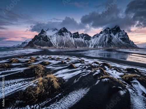 Snowy mountain peaks at sunrise, dramatic winter landscape with black sand dunes, majestic arctic wilderness scenery