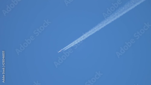 Jet aircraft cruising high with twin contrails stretching across blue sky, long distance flight route and aviation traffic concept. Exhaust plume forming linear cloud trail linked with atmospheric