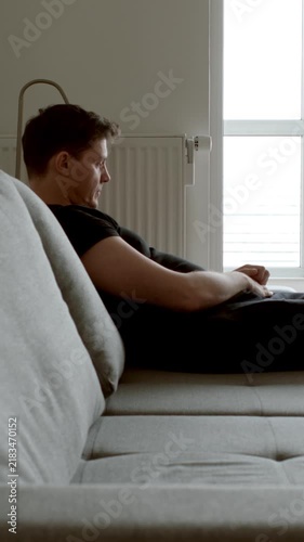 DEPRESSION: Sad young adult sits on a sofa at home
