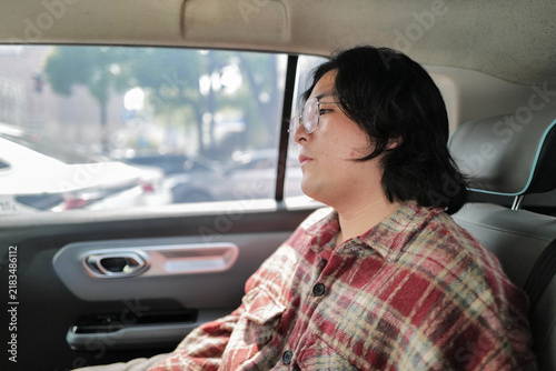 Photography A person in a plaid shirt sits in the back seat of a car beside a bright side window