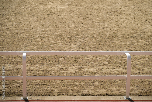 Empty horse racing track with sandy ground and white fence. Equestrian arena background for sport event, competition and training concept.