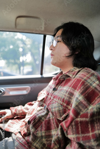 Photography A vertical view shows a person seated in the rear of a car beside the side window