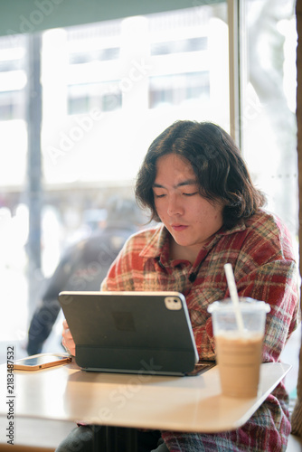 Canvas Print A vertical image shows a person using a tablet at a cafe table with a cold drink beside it