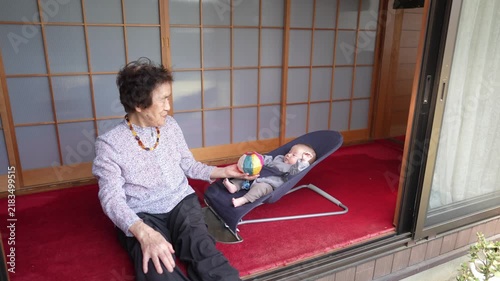 A seated person presents a multicolor patterned ball beside an infant reclining in a dark fabric bouncer.