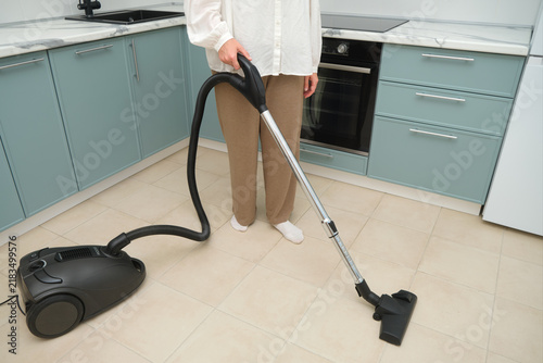Foto Woman vacuuming floor with modern vacuum cleaner in new kitchen