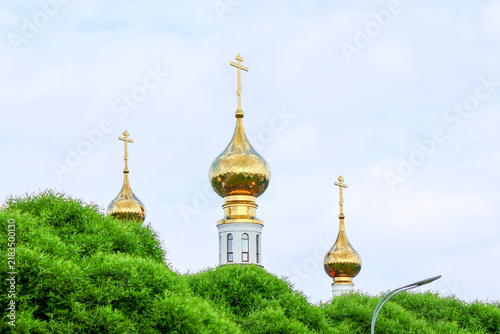 Photography Three ornate golden onion domes with crosses rise above lush green foliage again