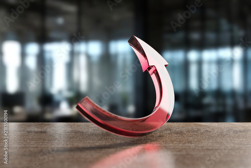 Фотография Red glass arrow sculpture on wooden table in modern office interior for design b