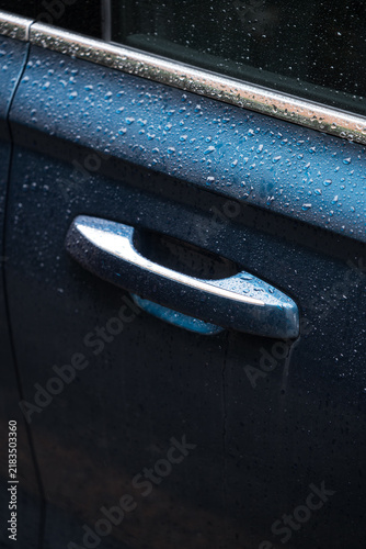 Modern car door handle close up with rain drops. Luxury automobile dark blue metallic body with wet water droplets pattern.