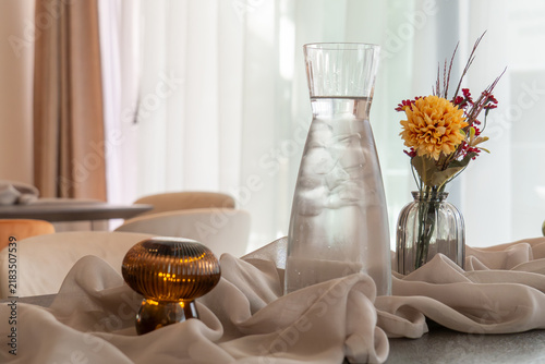 Fotografía Glass carafe with ice sits beside a small vase holding bright orange and purple flowers