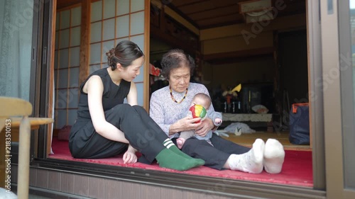 Two adults sit together at an open sliding doorway with an infant and a multicolor fabric ball.