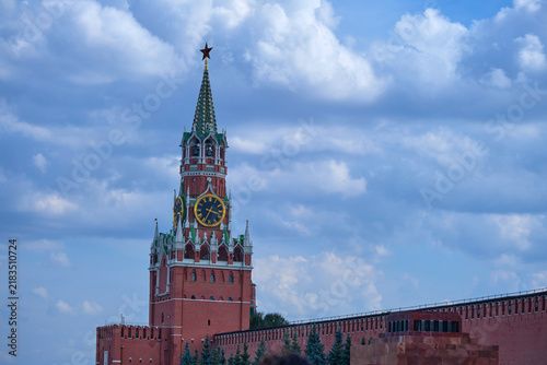 Historic Kremlin clock tower and red fortress wall beneath a dramatic blue sky. Moscow landmark and Russian architecture symbol for travel, history, culture, and tourism.