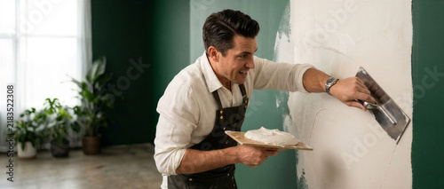 Man applying plaster on a wall with a hawk in a modern interior  