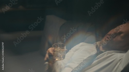 Caucasian middle aged businessman drinking whiskey from glass and falling asleep on couch. Footage suitable for mental health campaigns, addiction recovery programs, and workplace burnout awareness