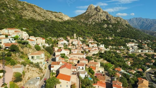 Lumio hilltop village aerial drone view facing Gulf of Calvi in Corsica France. Scenic perched medieval town in Balagne region mountains background 4K