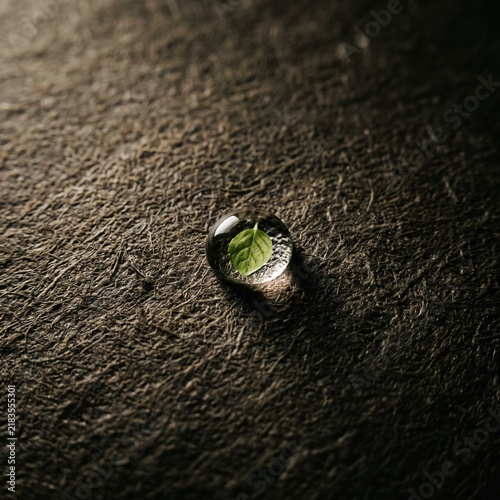 Macro photography of a single glowing water drop on a rough dark asphalt texture, tactile abstract background, deep natural contrast