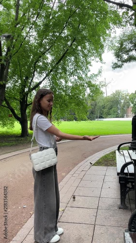 young woman feeds a great tit from her open palm beside a park bench as the wild bird perches close and takes food, illustrating trust, gentle interaction and connection with nature