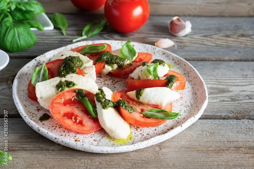 Caprese salad with juicy tomatoes, fresh mozzarella and pesto. Concept for a tasty and healthy appetizer, flat lay. Italian food, cuisine.