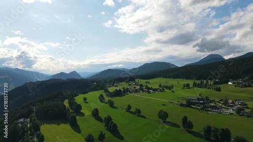 Aerial drone view of the idyllic countryside near Ramsau am Dachstein in Austria. Slow flight over lush green alpine meadows, traditional mountain houses and forests illuminated by warm summer evening