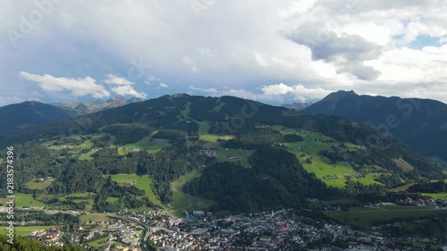 Aerial drone view of Planai mountain and the town of Schladming in the Austrian Alps. Summer sunlight illuminates the alpine landscape while dark storm clouds gather over the mountains